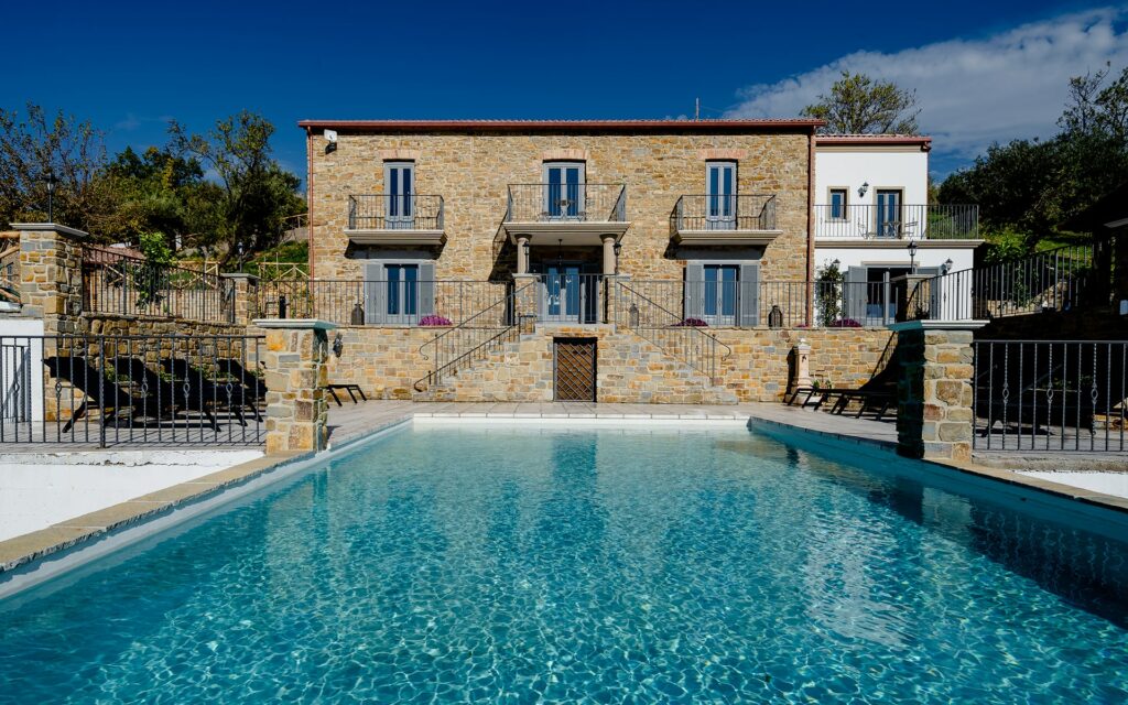 Stone house with 6 shuttered windows in front of swimming pool